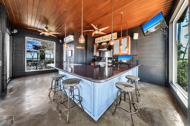 kitchen with pendant lighting, wooden ceiling, sink, wall chimney exhaust hood, and a kitchen bar