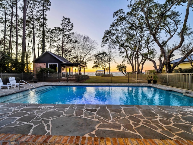 pool at dusk with a patio area and an outbuilding