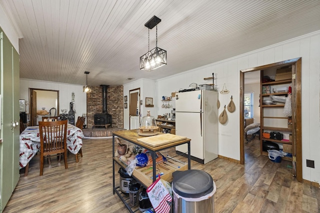 kitchen with hardwood / wood-style floors, pendant lighting, a wood stove, ornamental molding, and white fridge