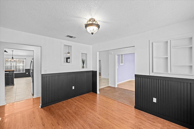 unfurnished living room featuring a notable chandelier, a textured ceiling, and hardwood / wood-style flooring