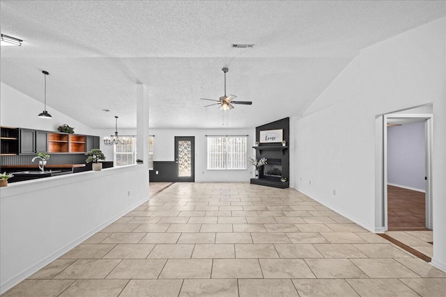 unfurnished living room featuring ceiling fan with notable chandelier, a textured ceiling, a large fireplace, and light tile patterned flooring