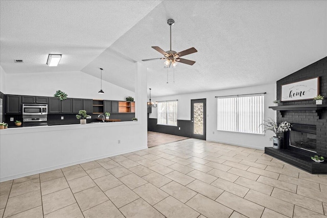 tiled living room featuring a textured ceiling, ceiling fan with notable chandelier, vaulted ceiling, and a brick fireplace