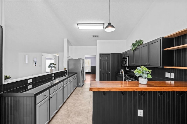 kitchen featuring kitchen peninsula, appliances with stainless steel finishes, lofted ceiling, and butcher block counters