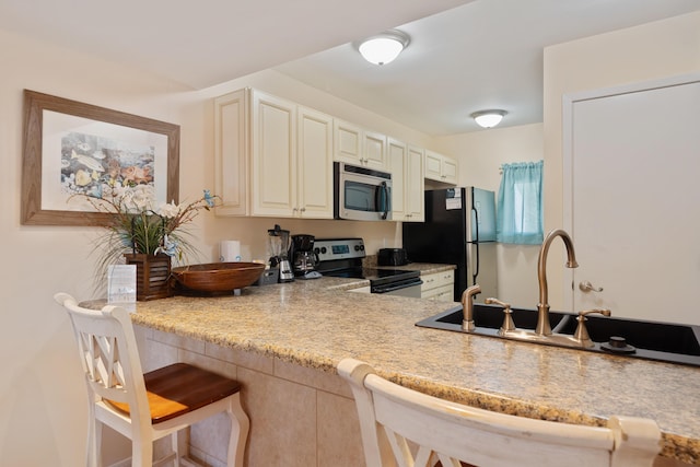 kitchen with cream cabinetry, a kitchen breakfast bar, light stone countertops, and black appliances