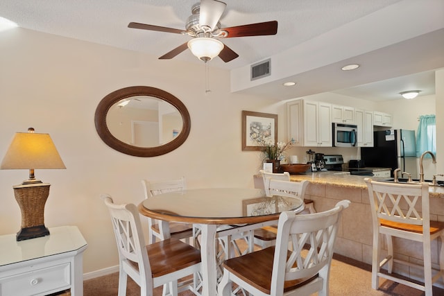 carpeted dining area with a textured ceiling, ceiling fan, and sink