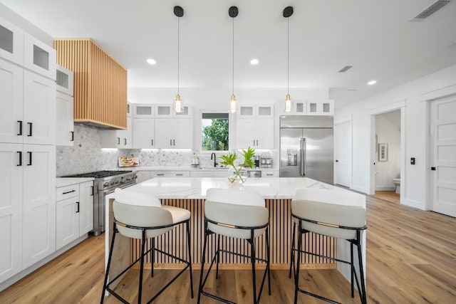 kitchen with premium appliances, a kitchen island, light hardwood / wood-style floors, and white cabinetry