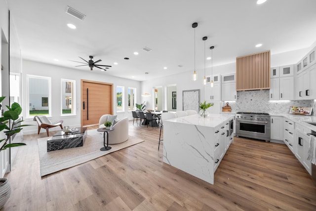 kitchen with white cabinetry, decorative light fixtures, high end stainless steel range oven, and light hardwood / wood-style floors