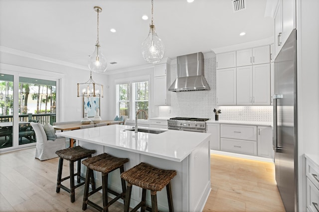 kitchen with a kitchen island with sink, sink, wall chimney range hood, high quality appliances, and white cabinets