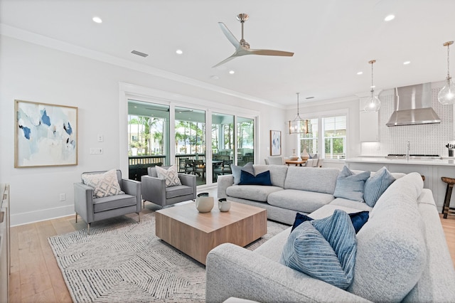 living room featuring crown molding, light hardwood / wood-style flooring, ceiling fan with notable chandelier, and sink