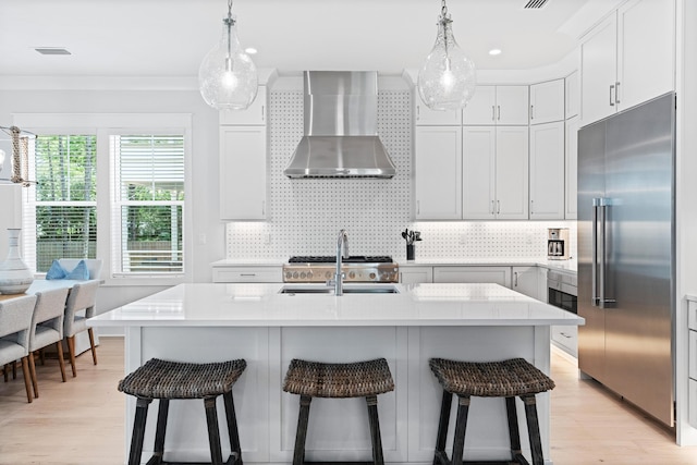 kitchen with an island with sink, stainless steel appliances, and wall chimney range hood