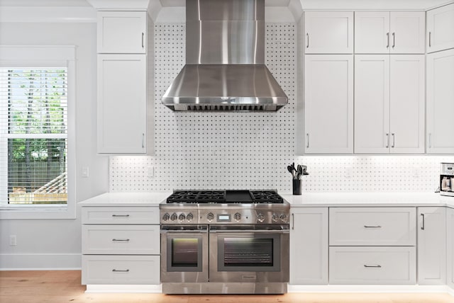 kitchen featuring double oven range, wall chimney exhaust hood, decorative backsplash, light hardwood / wood-style floors, and white cabinetry