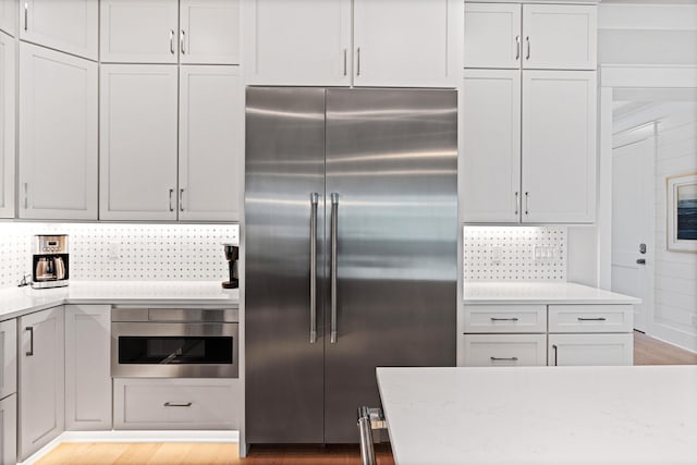 kitchen featuring decorative backsplash, light stone countertops, stainless steel appliances, white cabinets, and light hardwood / wood-style floors