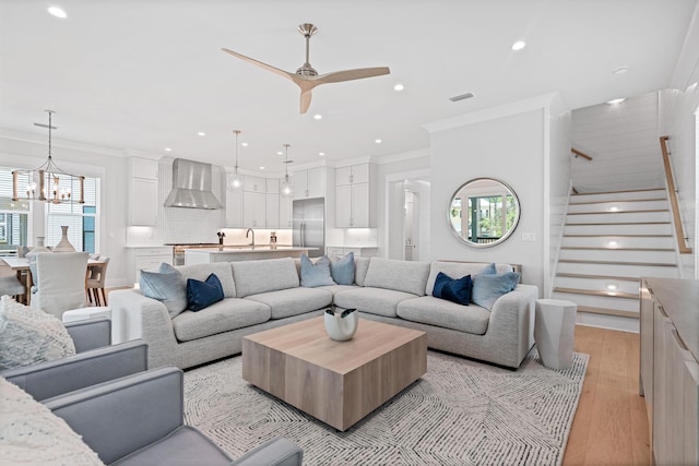 living room featuring ceiling fan with notable chandelier, light hardwood / wood-style floors, ornamental molding, and a wealth of natural light