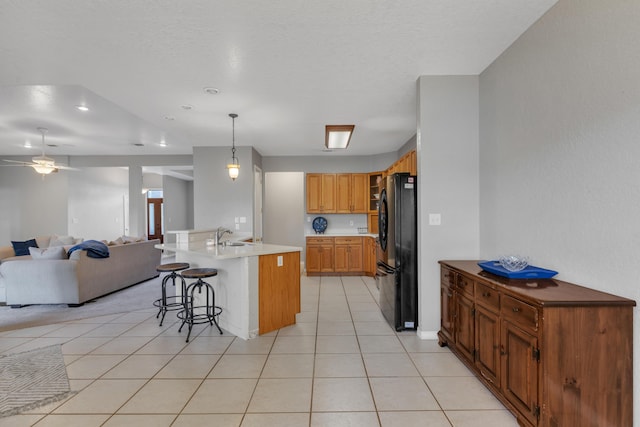 kitchen with black fridge, pendant lighting, a kitchen island with sink, a breakfast bar, and light tile patterned floors