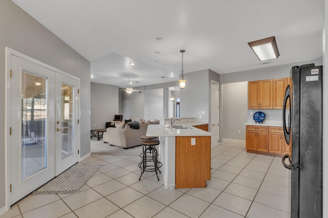 kitchen featuring a kitchen breakfast bar, refrigerator, ceiling fan, a kitchen island with sink, and hanging light fixtures