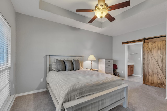 carpeted bedroom with ceiling fan, a barn door, ensuite bathroom, and a tray ceiling