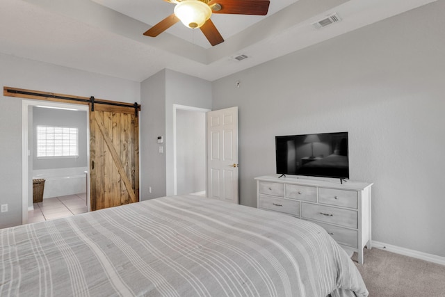 bedroom with a barn door, ceiling fan, ensuite bath, and light colored carpet