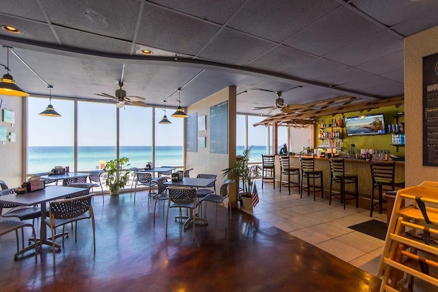 dining room featuring tile patterned floors, bar, ceiling fan, and a wall of windows