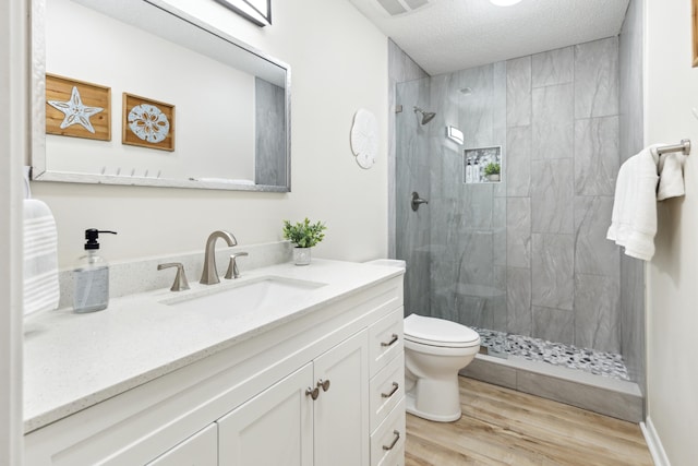 bathroom with vanity, a textured ceiling, tiled shower, toilet, and hardwood / wood-style flooring