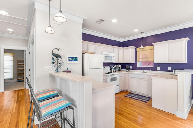 kitchen featuring a kitchen breakfast bar, kitchen peninsula, pendant lighting, white appliances, and white cabinets