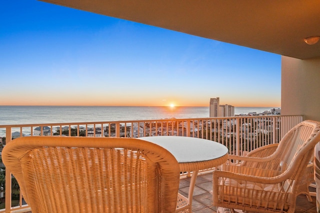 balcony at dusk featuring a water view and a view of the beach