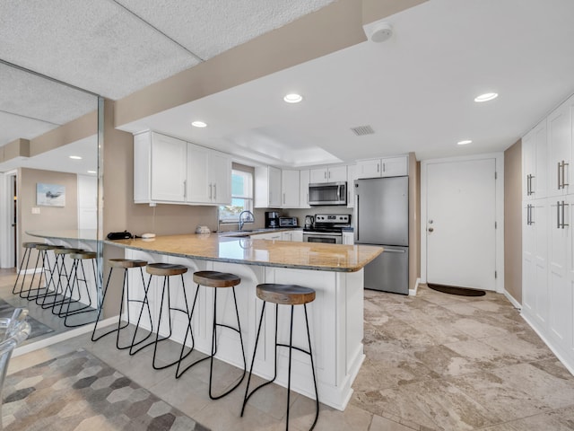 kitchen with white cabinets, appliances with stainless steel finishes, sink, a kitchen breakfast bar, and kitchen peninsula