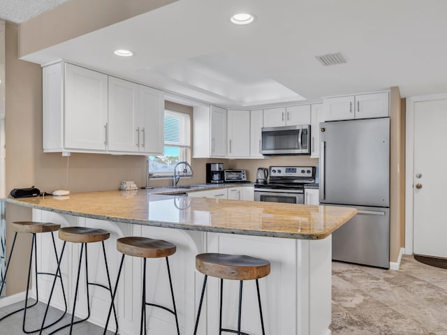 kitchen with appliances with stainless steel finishes, white cabinets, kitchen peninsula, and a tray ceiling