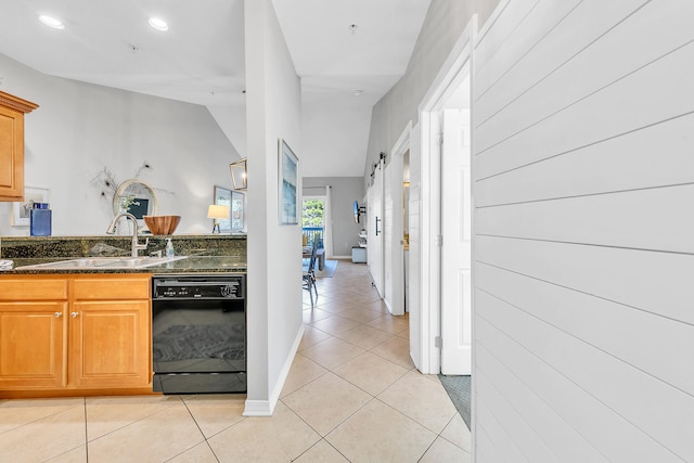 kitchen featuring sink, vaulted ceiling, a barn door, dark stone countertops, and black dishwasher