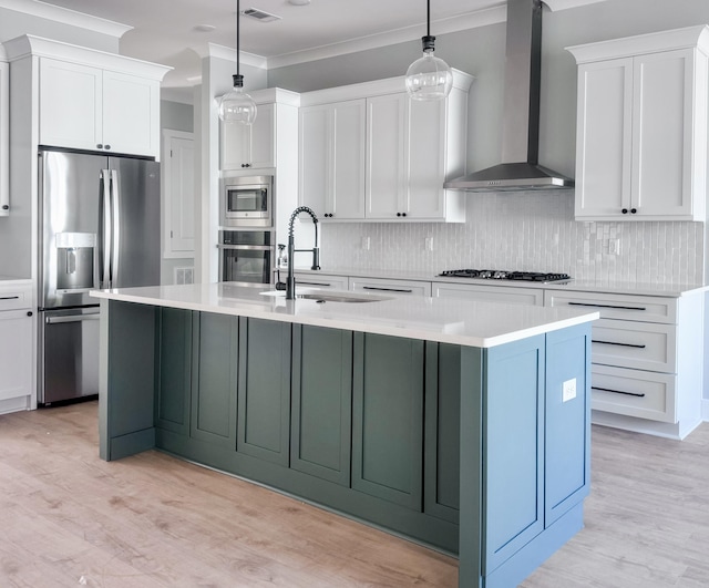 kitchen featuring light wood-type flooring, wall chimney exhaust hood, stainless steel appliances, sink, and hanging light fixtures