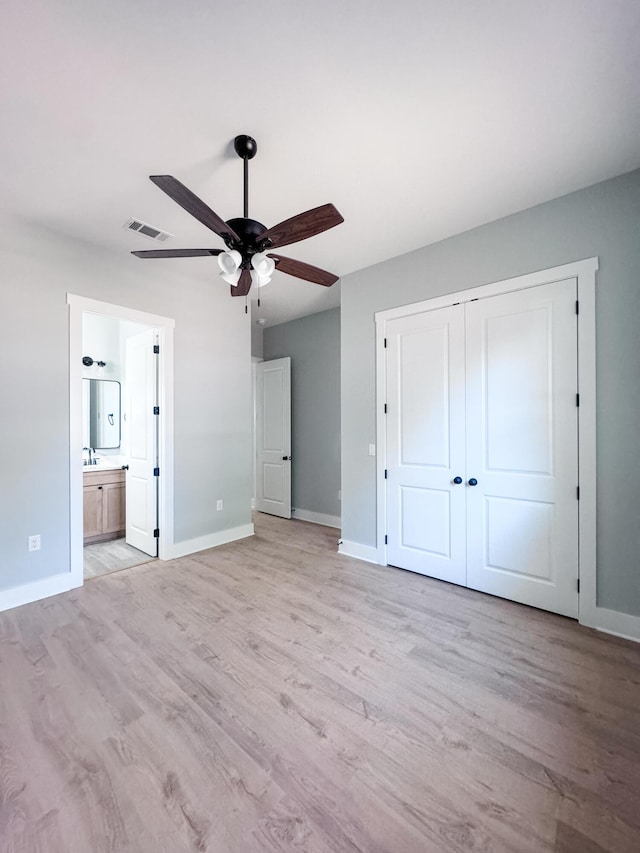 unfurnished bedroom with light wood-type flooring, a closet, ensuite bath, and ceiling fan