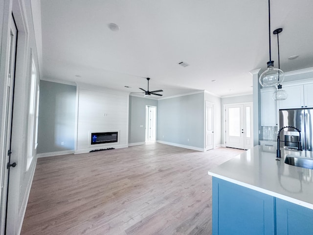 unfurnished living room featuring a large fireplace, light wood-type flooring, sink, and ornamental molding