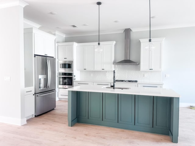 kitchen with sink, hanging light fixtures, wall chimney range hood, a center island with sink, and appliances with stainless steel finishes