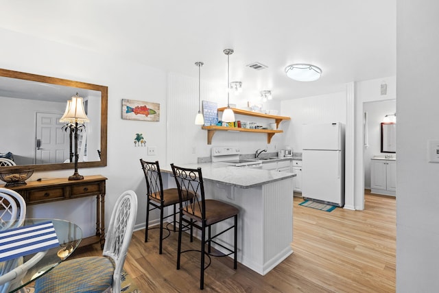 kitchen with a kitchen breakfast bar, kitchen peninsula, white appliances, and light wood-type flooring