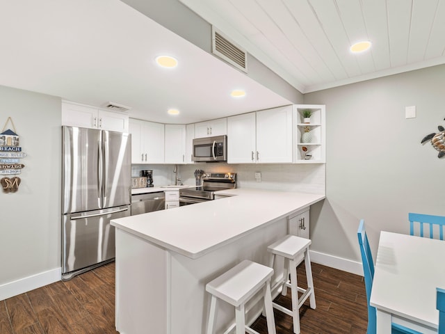 kitchen featuring dark wood-type flooring, kitchen peninsula, appliances with stainless steel finishes, a kitchen bar, and white cabinetry