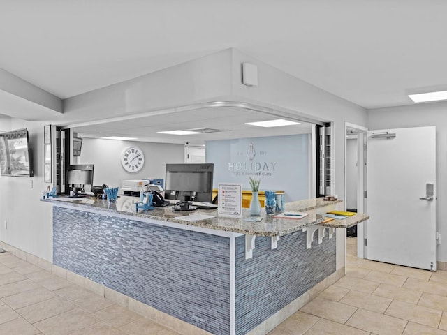 kitchen featuring kitchen peninsula, light tile patterned floors, light stone counters, and a breakfast bar area