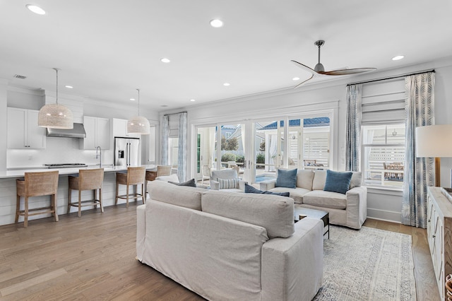 living room featuring light hardwood / wood-style flooring, a wealth of natural light, crown molding, and ceiling fan