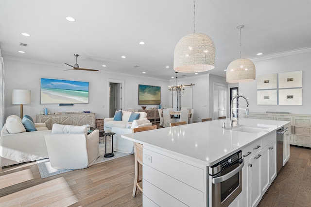 kitchen featuring appliances with stainless steel finishes, sink, white cabinetry, hanging light fixtures, and an island with sink