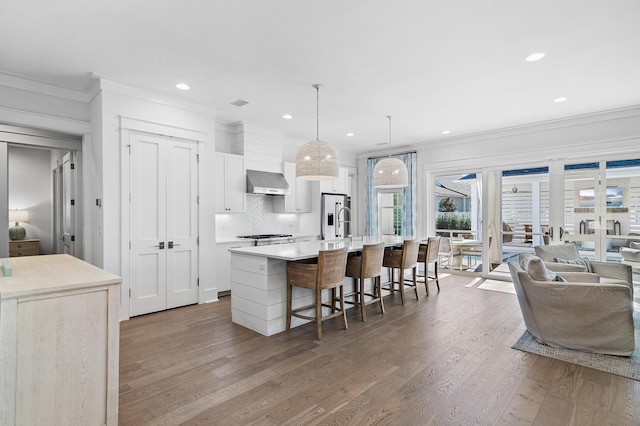 kitchen with wall chimney exhaust hood, a spacious island, decorative light fixtures, hardwood / wood-style flooring, and white cabinets