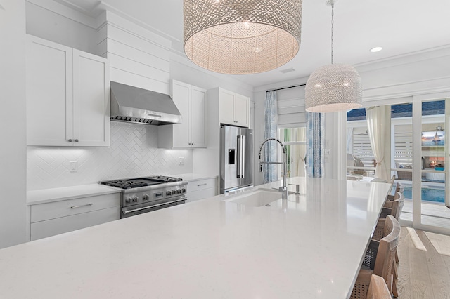 kitchen with high quality appliances, a kitchen breakfast bar, wood-type flooring, wall chimney exhaust hood, and white cabinetry