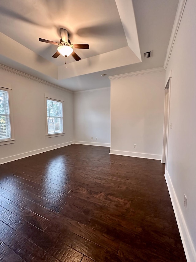 empty room featuring a tray ceiling, a wealth of natural light, dark hardwood / wood-style flooring, and crown molding