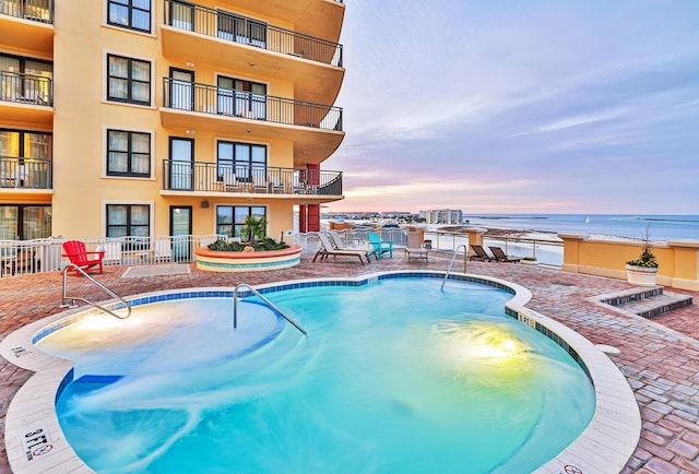 pool at dusk featuring a water view and a patio