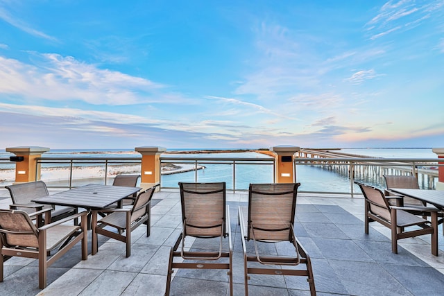 patio terrace at dusk featuring a water view and a beach view