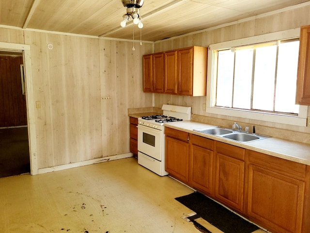 kitchen with white range with gas stovetop, sink, wooden ceiling, and wood walls