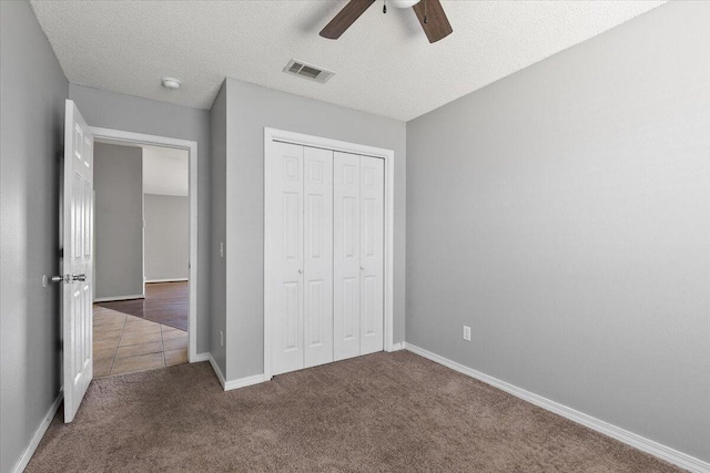 unfurnished bedroom featuring dark colored carpet, a textured ceiling, a closet, and ceiling fan