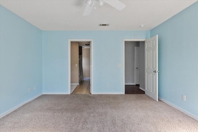 unfurnished bedroom featuring ceiling fan, light colored carpet, a textured ceiling, and connected bathroom