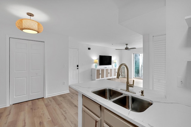 kitchen with pendant lighting, sink, ceiling fan, light wood-type flooring, and light stone counters