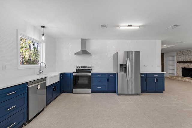 kitchen featuring pendant lighting, a stone fireplace, sink, wall chimney exhaust hood, and stainless steel appliances