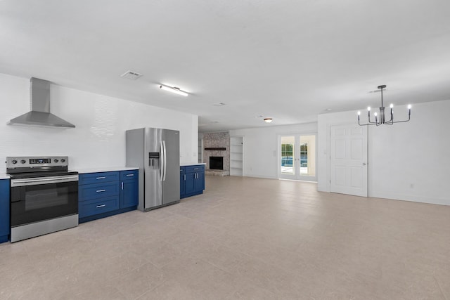 kitchen with blue cabinetry, wall chimney exhaust hood, a stone fireplace, a notable chandelier, and appliances with stainless steel finishes