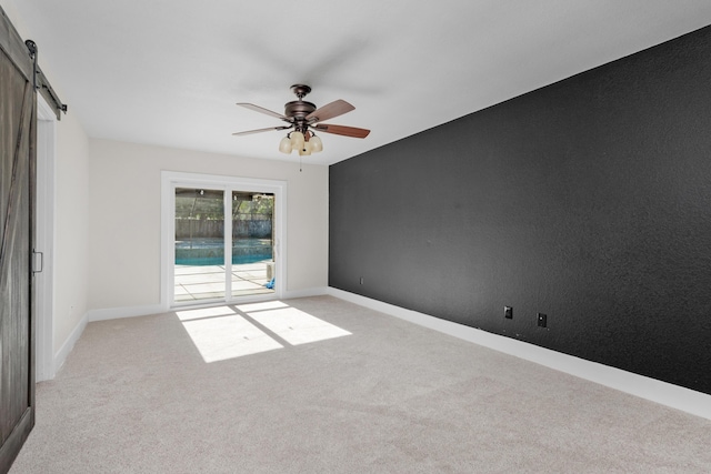 carpeted spare room featuring ceiling fan and a barn door