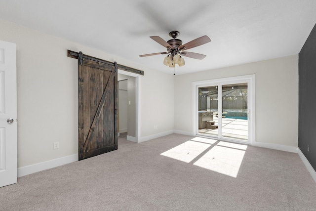 unfurnished room featuring light carpet, a barn door, and ceiling fan